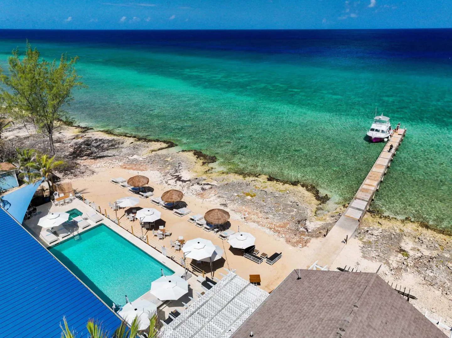 Aerial view of pool, beach, pier, and boat at Cobalt Coast Resort.