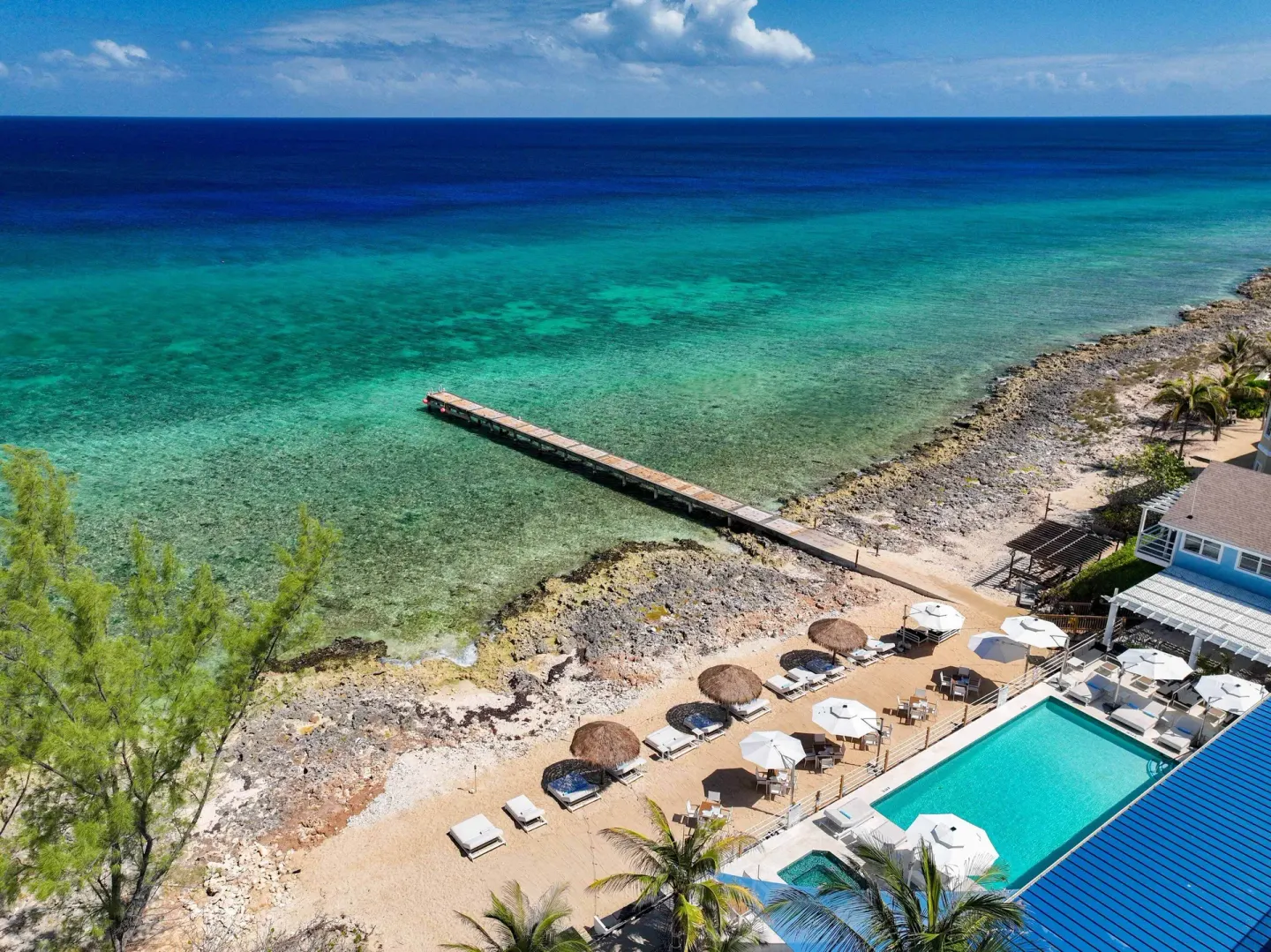 Aerial view of the pool, rocky shoreline, pier, and turquoise sea at Cobalt Coast Resort.