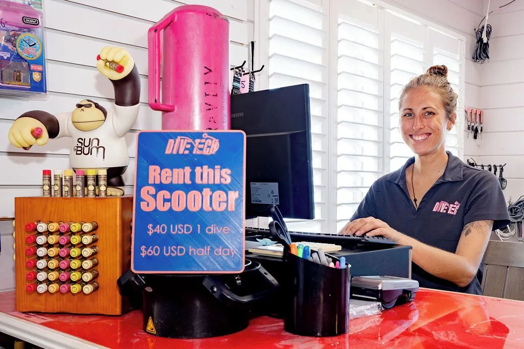Dive shop counter with staff member and scooter rental sign at Cobalt Coast Resort.