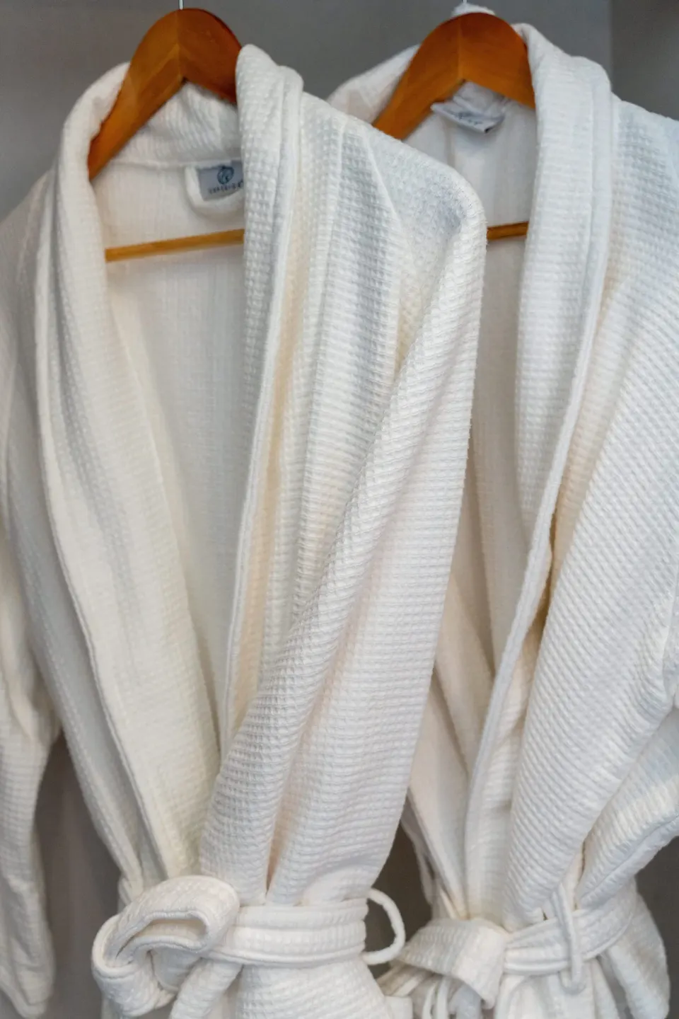 Two white waffle robes hanging on wooden hangers at Cobalt Coast Resort.