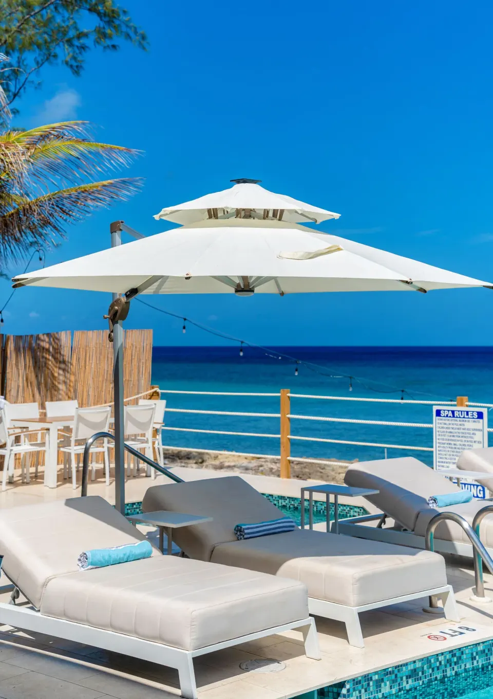 Pool loungers with towels sit under a white umbrella beside the sea at Cobalt Coast Resort.