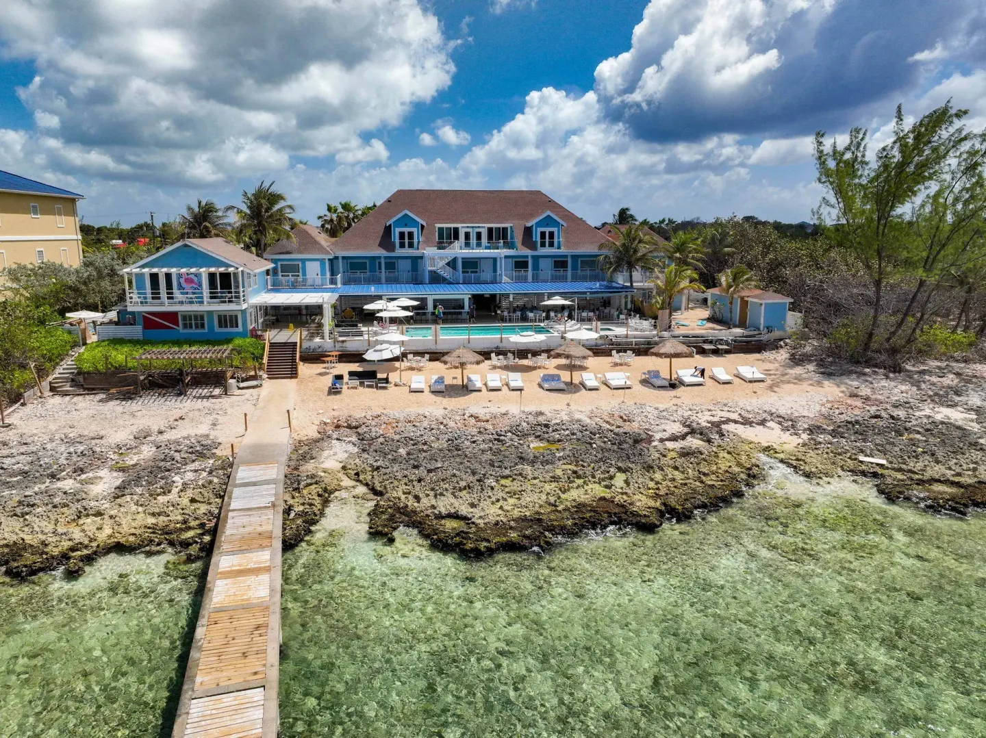 Seaward view of Cobalt Coast Resort with a pier, rocky shore, pool deck, and beach loungers.