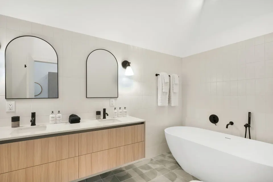 Signature Room bathroom with double vanity, arched mirrors, towels, and soaking tub at Cobalt Coast Resort.