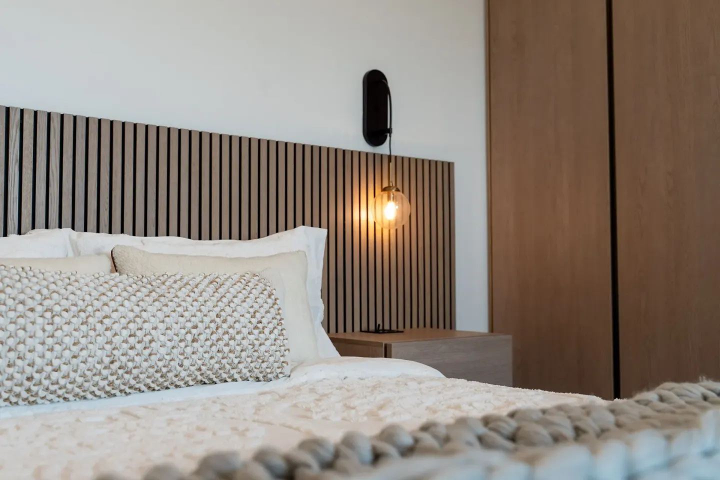 Signature Room king bed detail with pillows, slat headboard, sconce, and wardrobe at Cobalt Coast Resort.