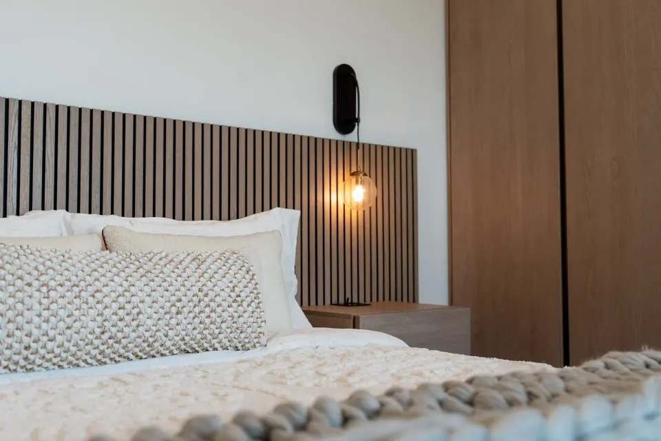 Signature Room king bed detail with pillows, slat headboard, sconce, and wardrobe at Cobalt Coast Resort.