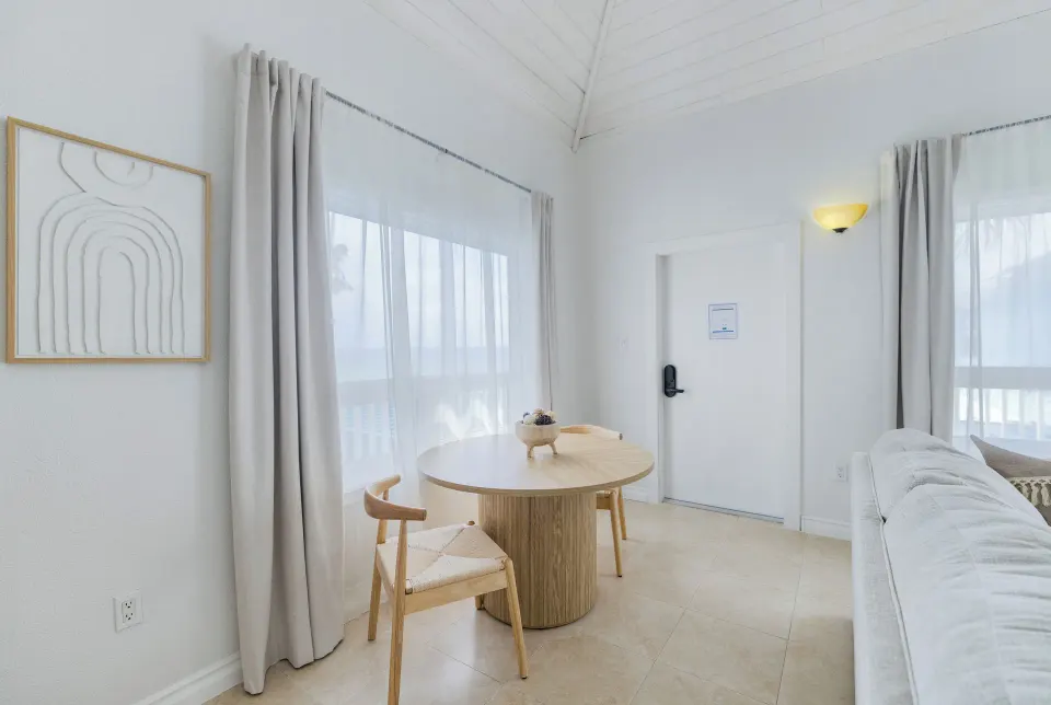 One Bedroom Suite dining nook with round table, two chairs, and curtained windows at Cobalt Coast Resort.