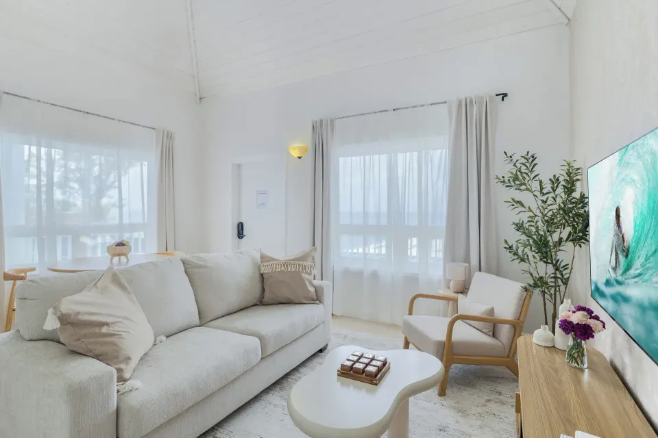 One Bedroom Suite living room with sofa, TV, chair, coffee table, and sheer curtains at Cobalt Coast Resort.