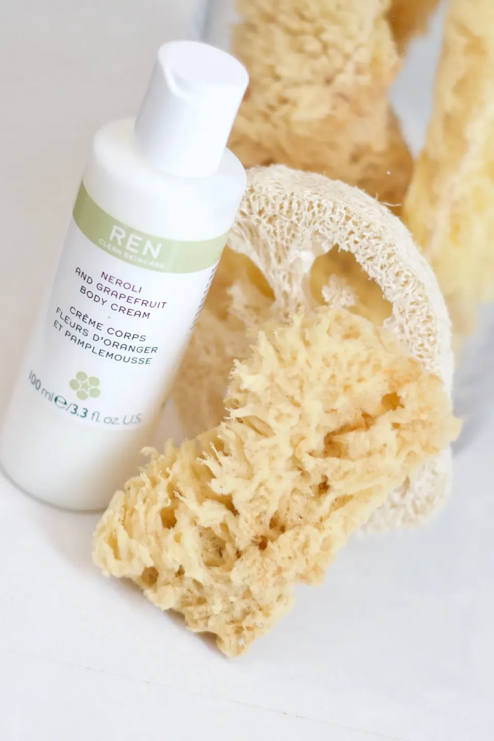 Bathroom body cream bottle and natural sponges on a white surface at Cobblers Cove.