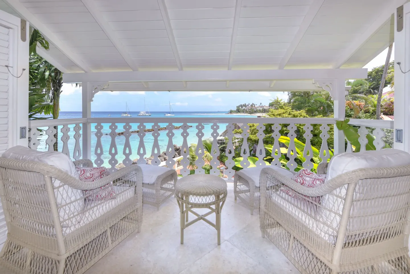 Covered balcony with white wicker chairs overlooking the bay at Cobblers Cove.