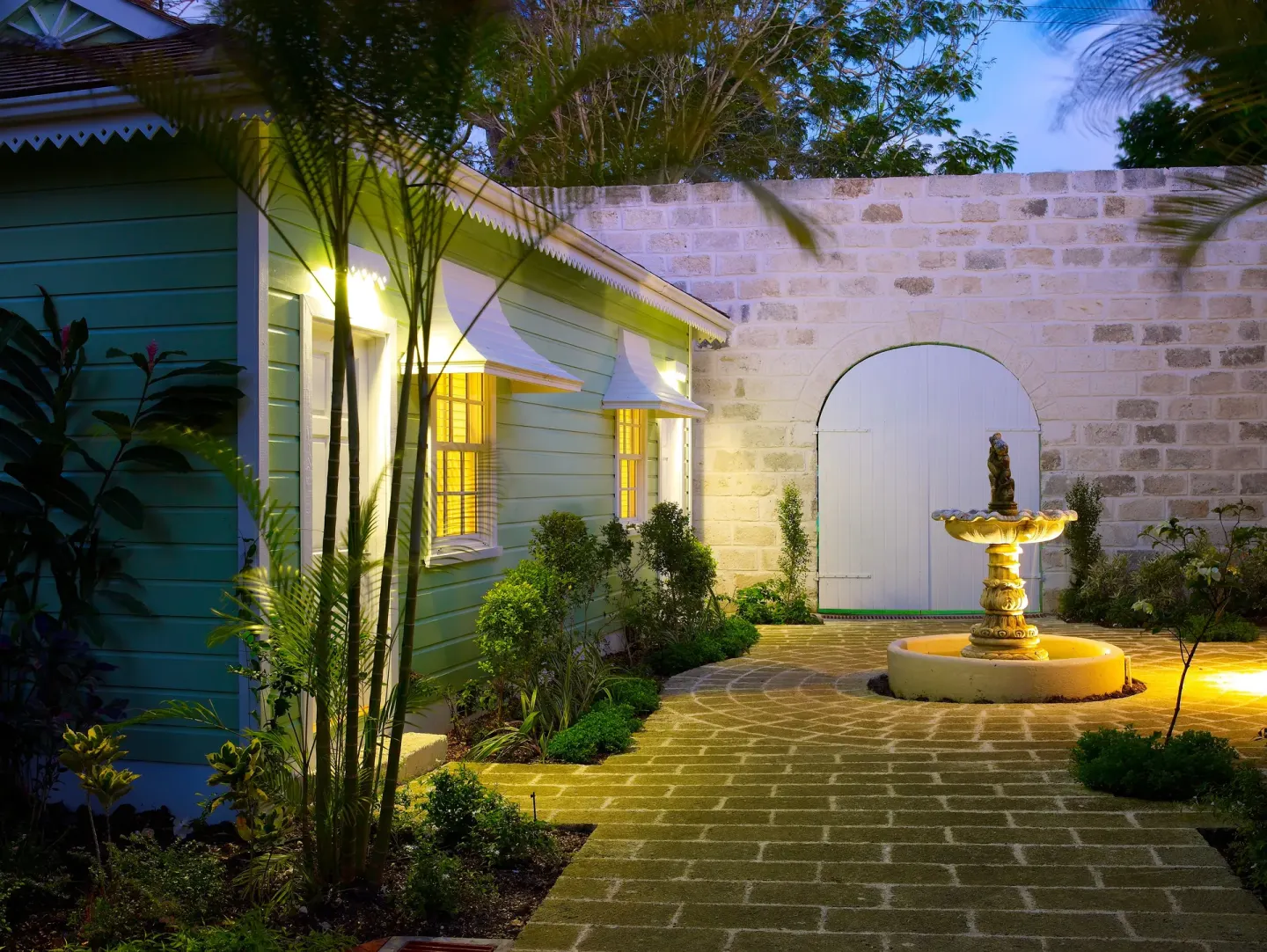 Evening courtyard with fountain, stone wall, and lit cottage windows at Cobblers Cove.