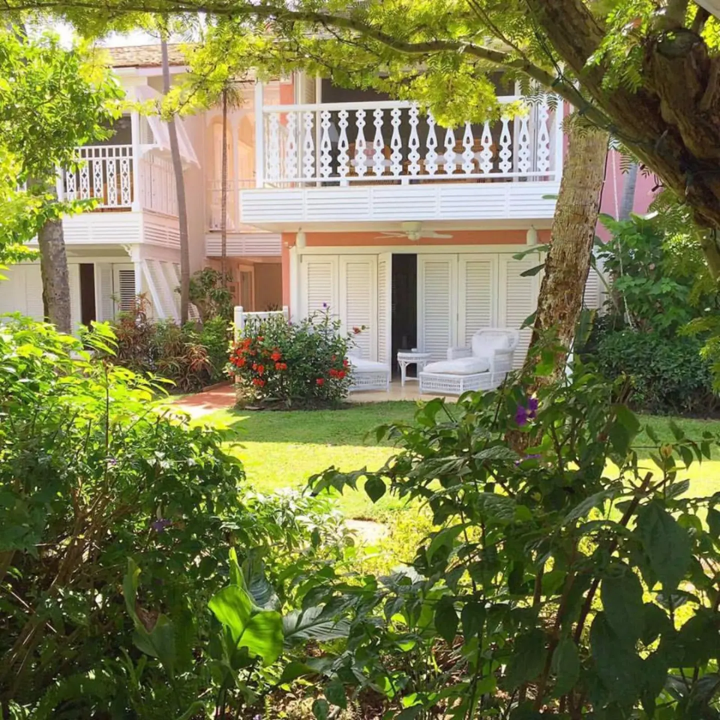 Pink resort building with white balconies seen through gardens at Cobblers Cove.