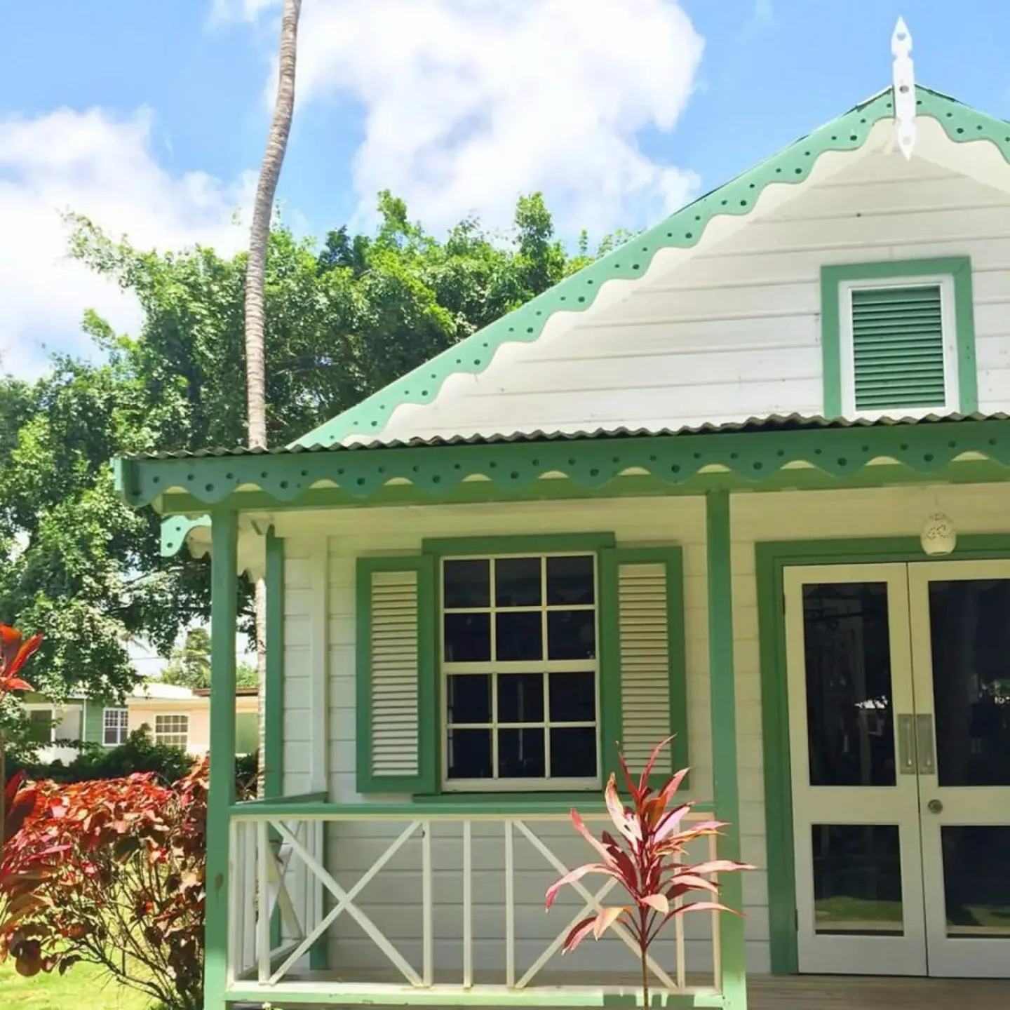White cottage exterior with green trim and tropical plants at Cobblers Cove.