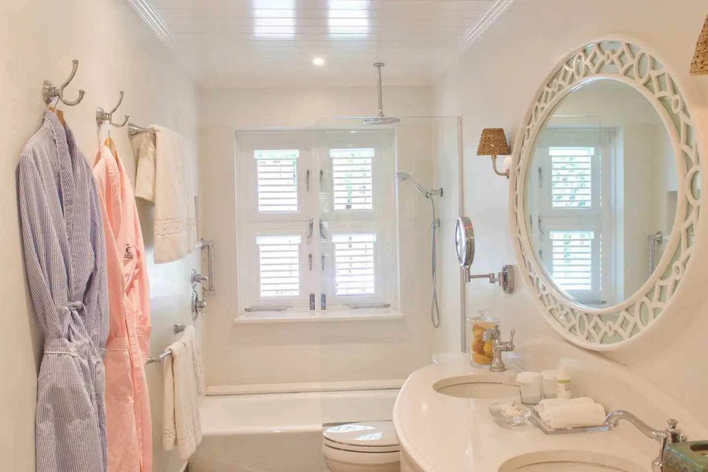 Bathroom with double vanity, round mirror, robes and glass shower at Cobblers Cove.
