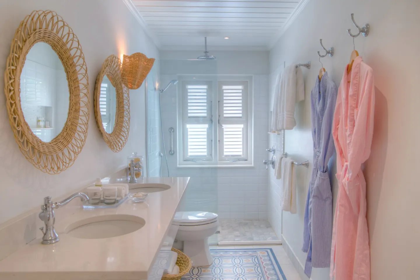 Bathroom with woven mirrors, double sinks, robes and shower at Cobblers Cove.