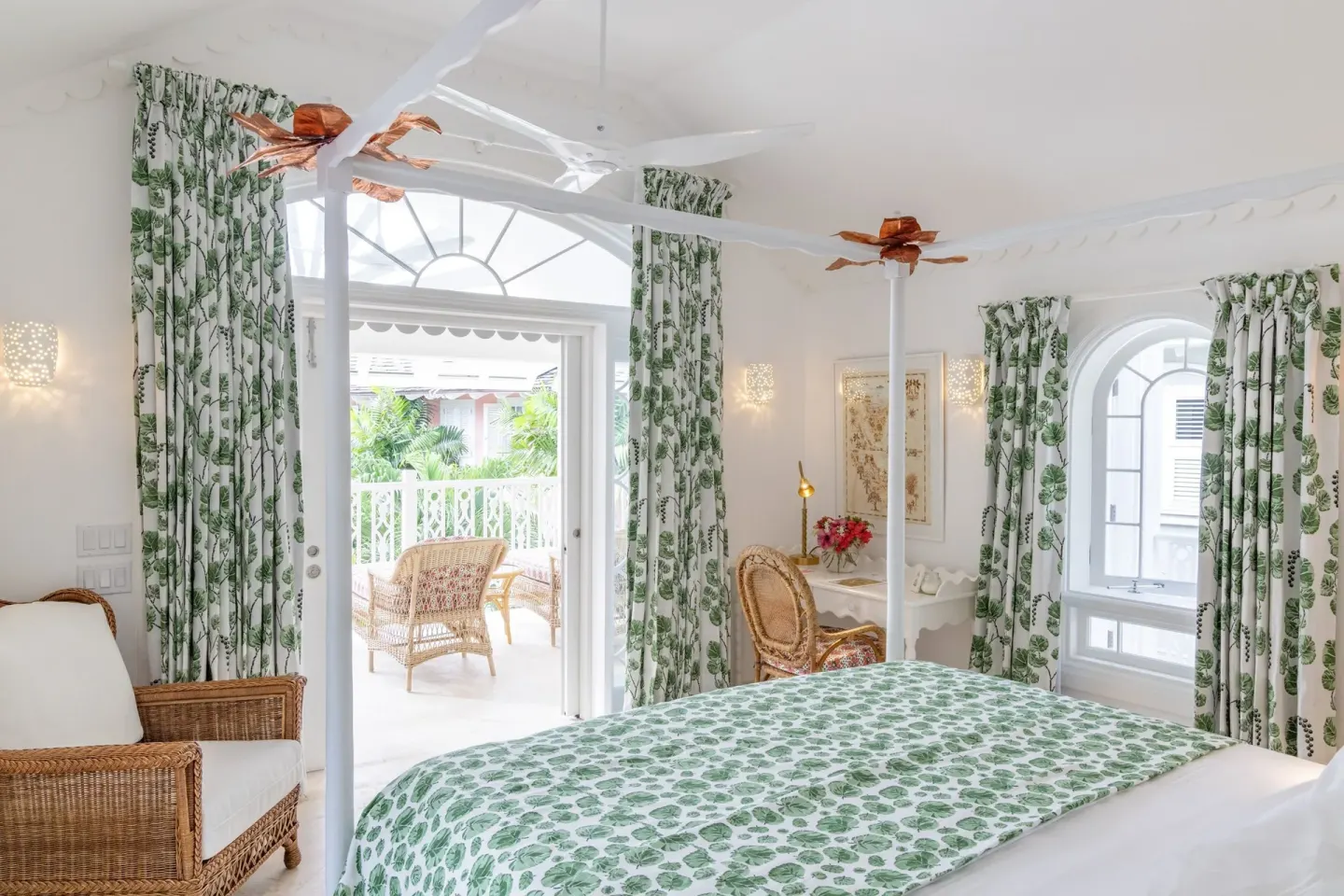 Guest room bed beside open balcony doors with wicker seating at Cobblers Cove.