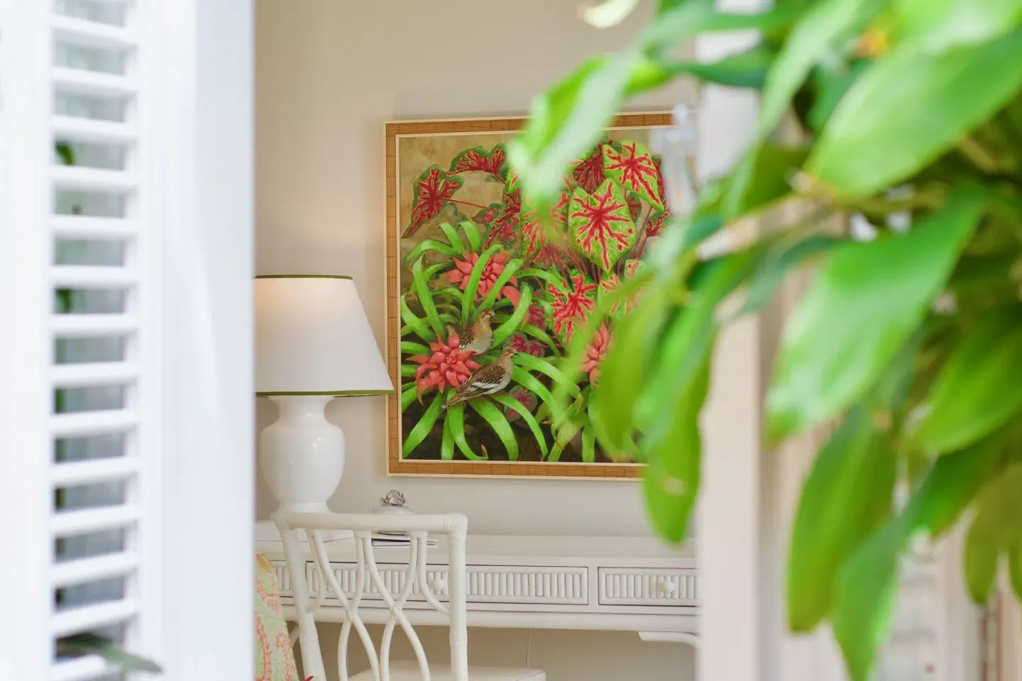 Guest room artwork and desk partly framed by tropical leaves at Cobblers Cove.