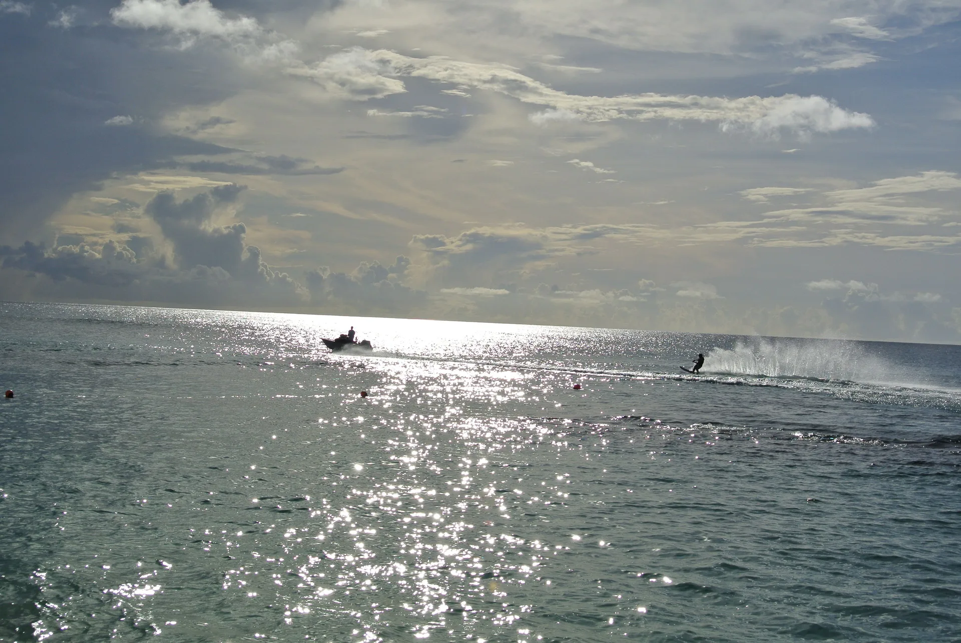 Sunlit ocean with a small boat and water skier offshore from Cobblers Cove.