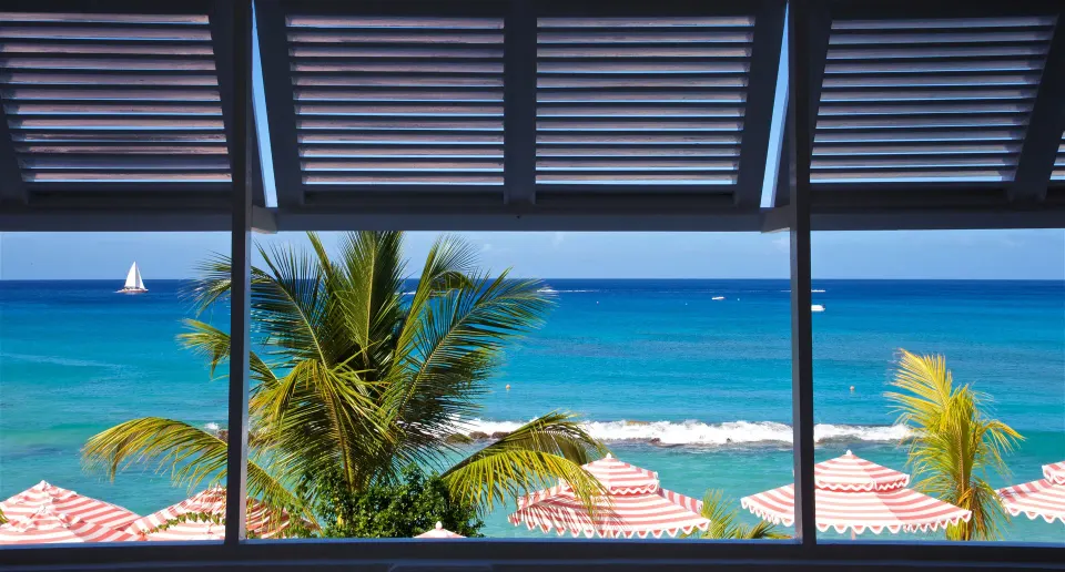 Sea view from Camelot at the Great House at Cobblers Cove with palms, umbrellas and sailboats.