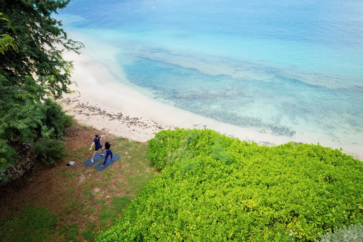 Aerial view of two guests on yoga mats above the beach at Cocobay Resort.