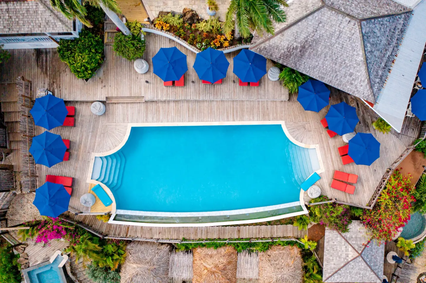 Aerial view of a pool deck with blue umbrellas and red loungers at Cocobay Resort.