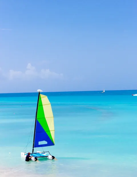 A small sailboat sits in shallow turquoise water near Cocobay Resort.
