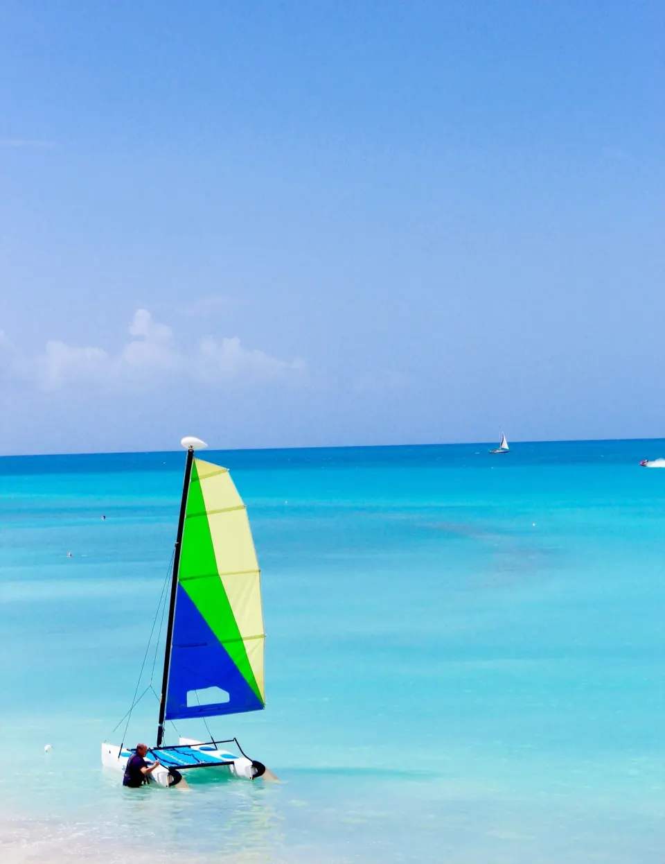 A small sailboat sits in shallow turquoise water near Cocobay Resort.