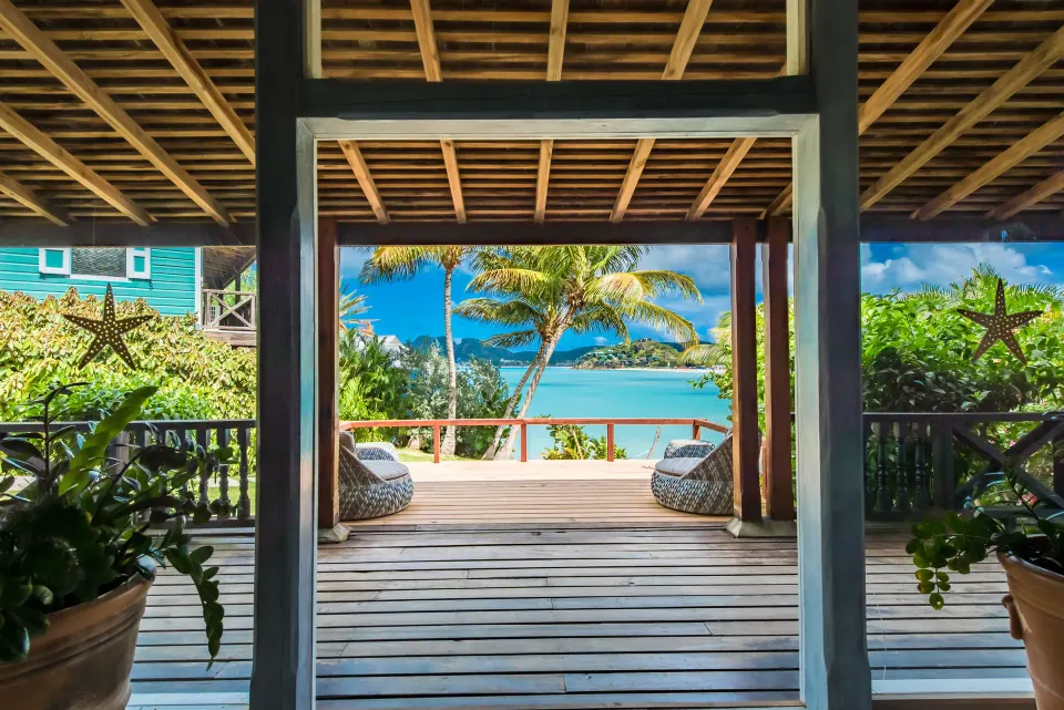 A covered wooden deck frames palm trees and the sea at Cocobay Resort.