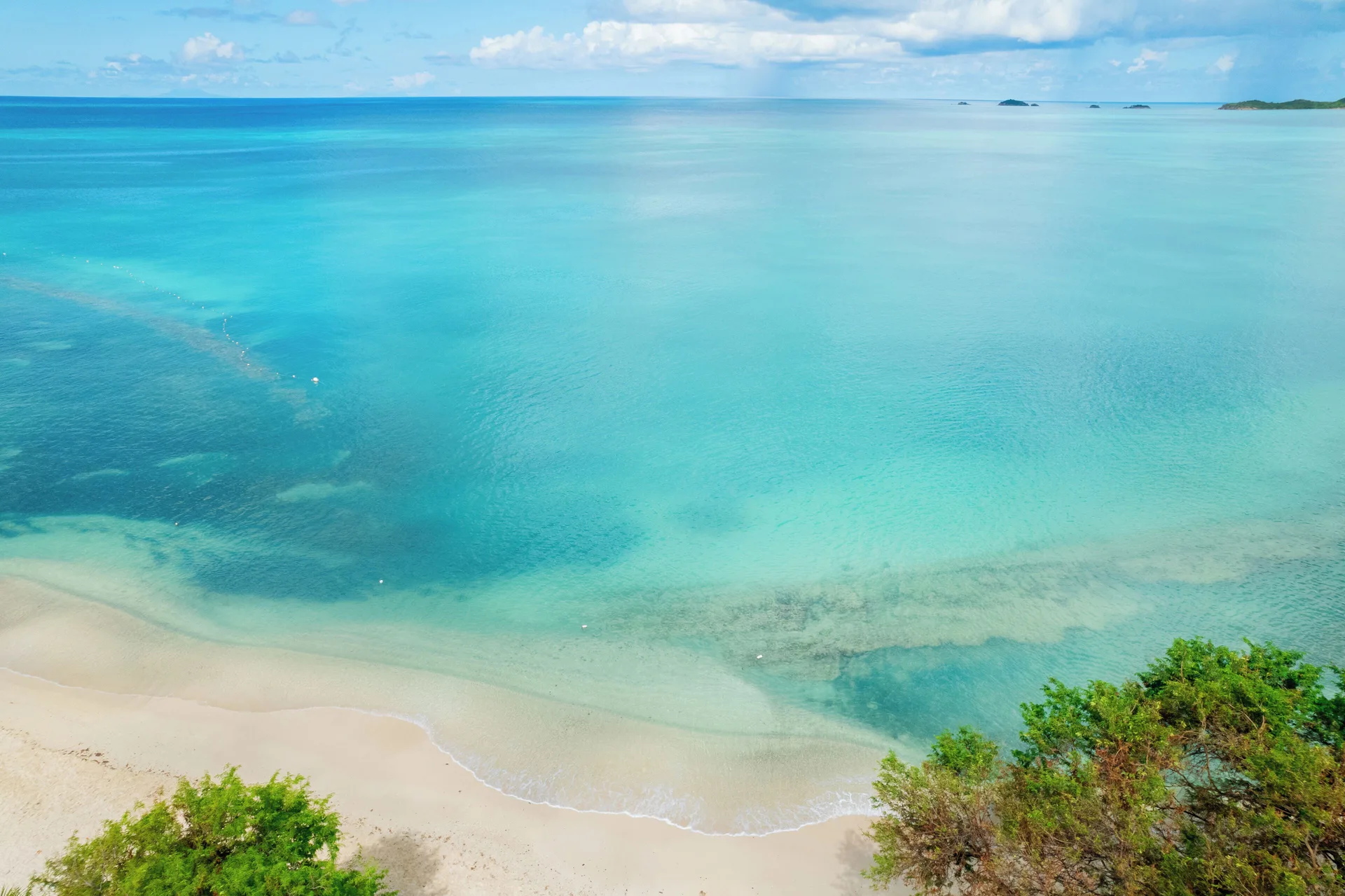 Elevated view of clear turquoise water and a sandy shoreline at Cocobay Resort.