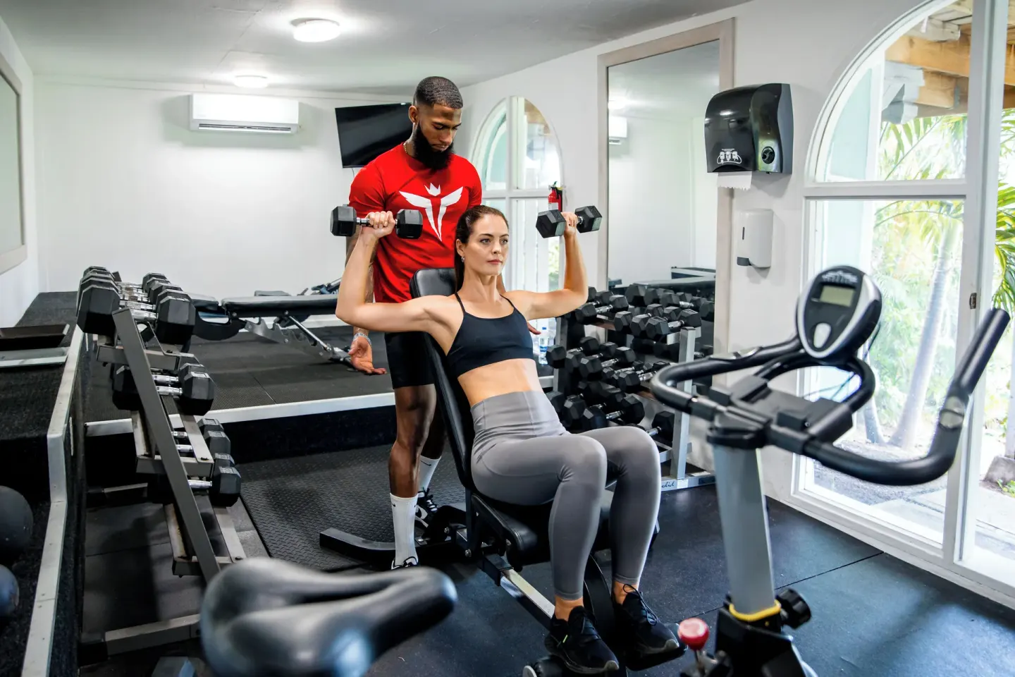 Guest lifting dumbbells with a trainer in the fitness room at Cocobay Resort.