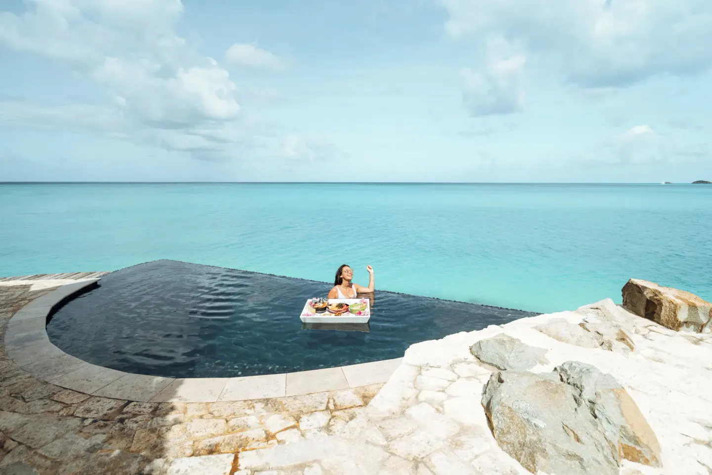 Guest in a dark infinity pool with floating breakfast and sea view at Cocobay Resort.