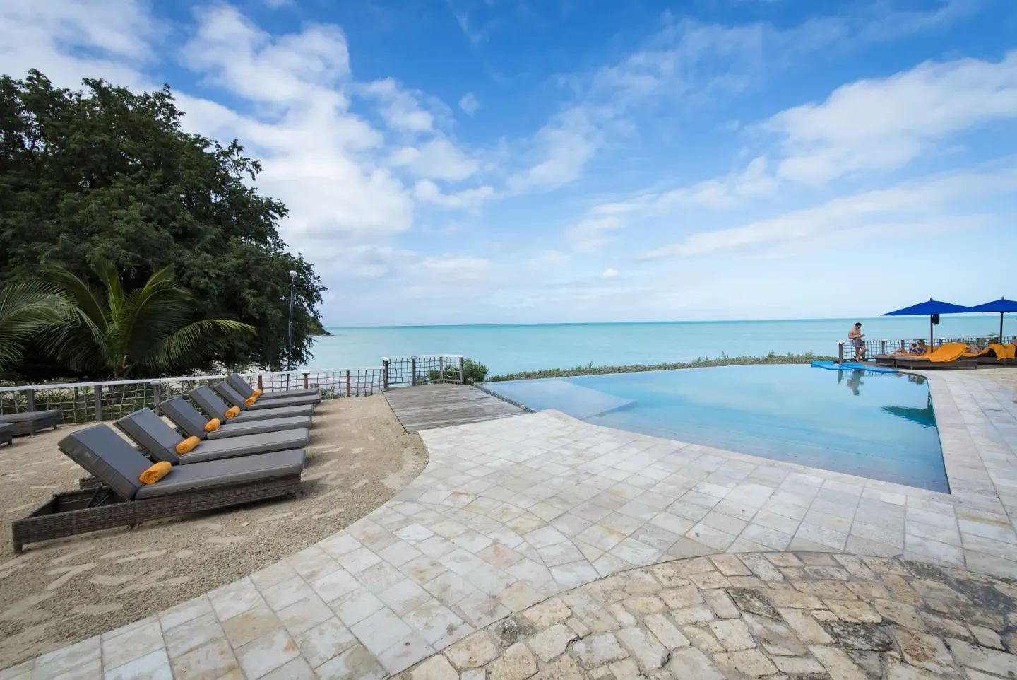 Infinity pool with loungers, trees, and calm sea beyond at Cocobay Resort.
