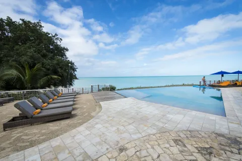 Infinity pool with loungers, trees, and calm sea beyond at Cocobay Resort.