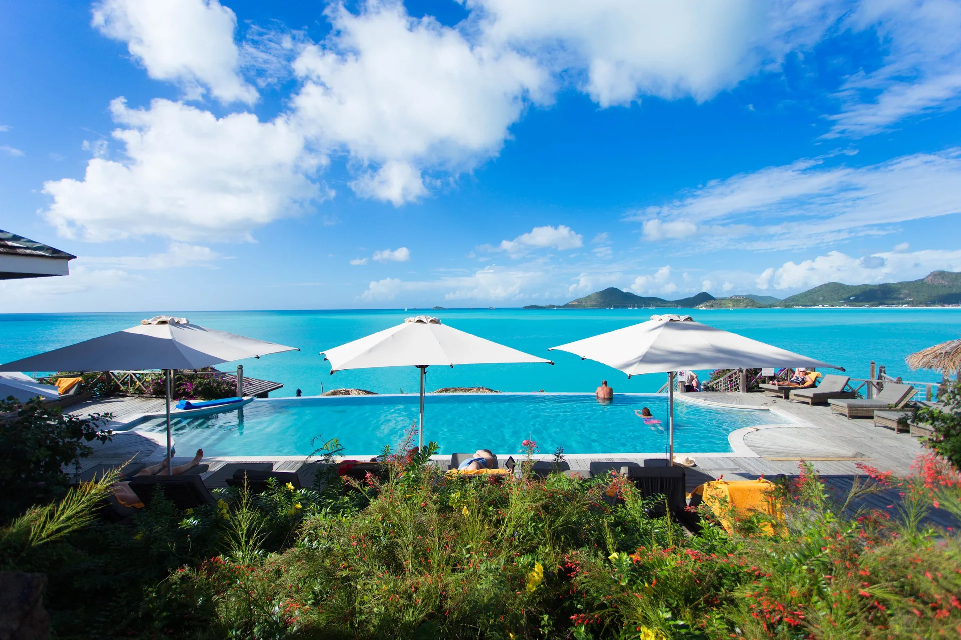 Infinity pool with white umbrellas overlooking turquoise water at Cocobay Resort.