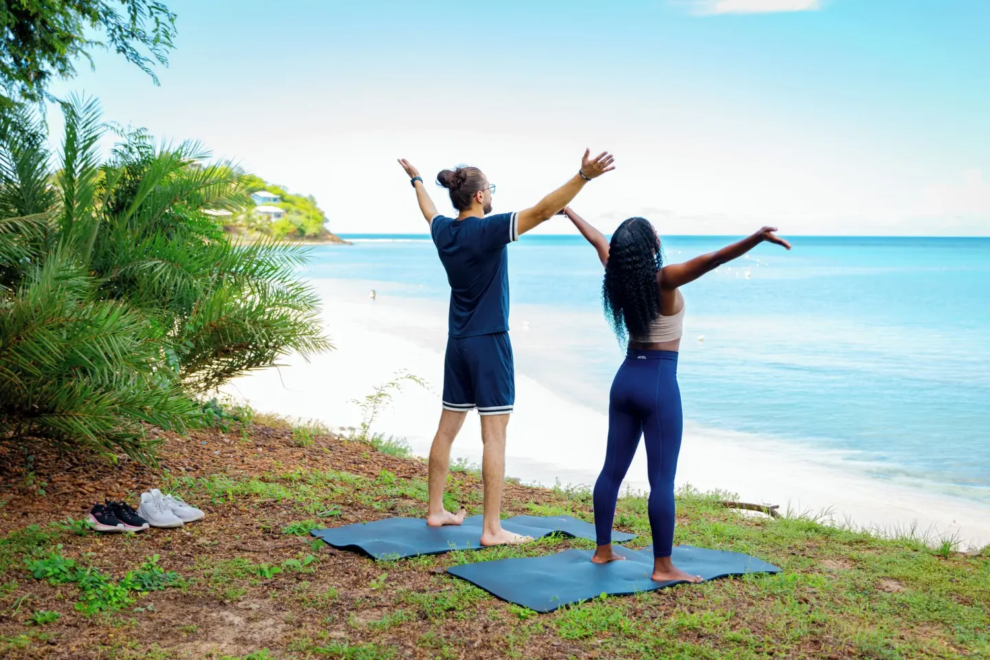 Two guests stretching on yoga mats above the beach at Cocobay Resort.