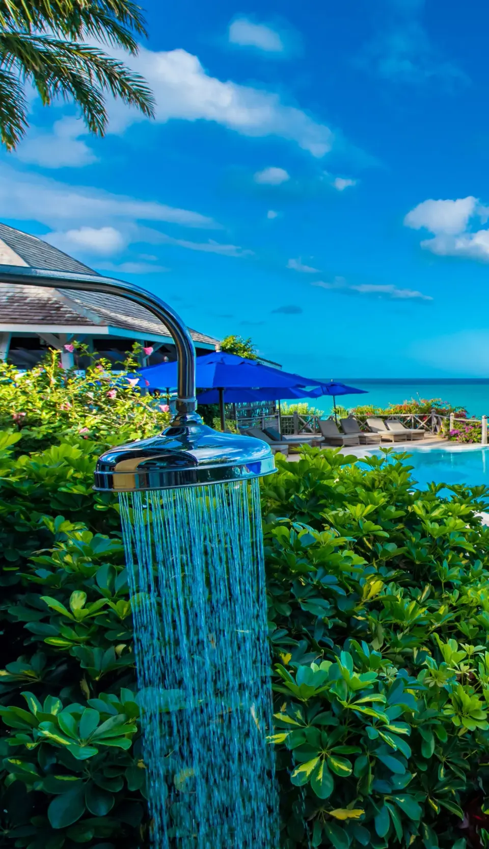 Outdoor shower running beside the pool and greenery at Cocobay Resort.