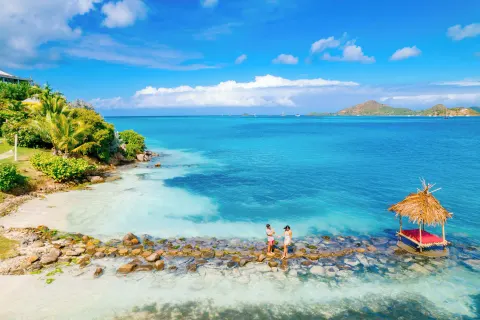 Aerial view of a rocky shoreline, thatched platform, and blue bay at Cocobay Resort.