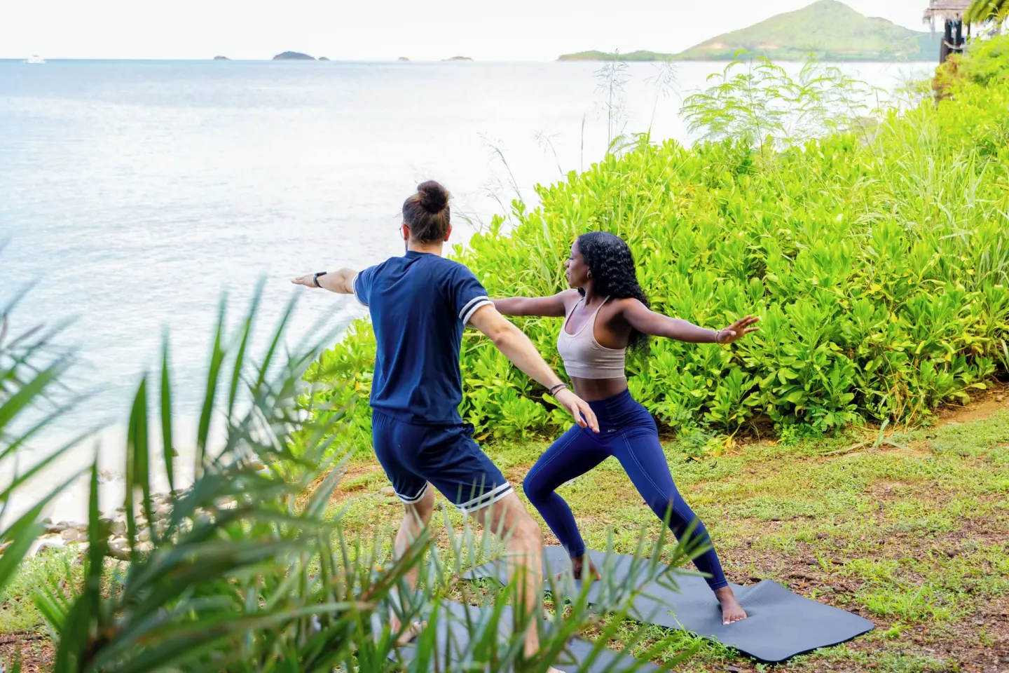 Two guests doing yoga on mats by the shoreline at Cocobay Resort.