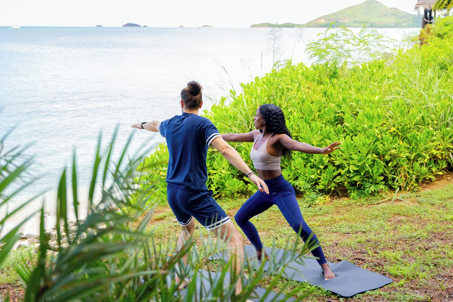 Two guests doing yoga on mats by the shoreline at Cocobay Resort.