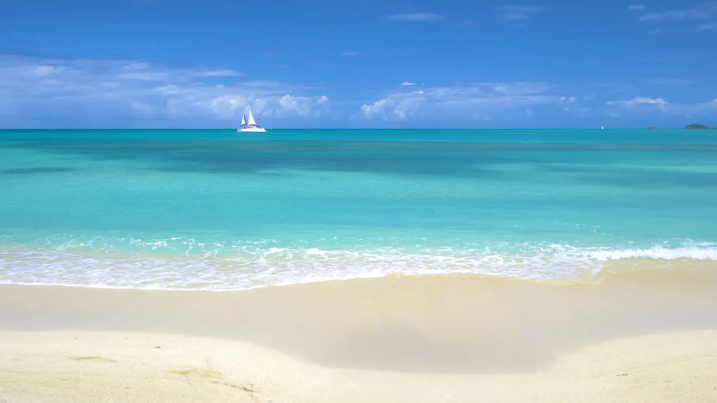 A calm turquoise beach with a sailboat offshore at Cocobay Resort.