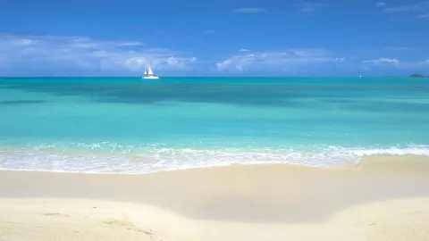 A calm turquoise beach with a sailboat offshore at Cocobay Resort.