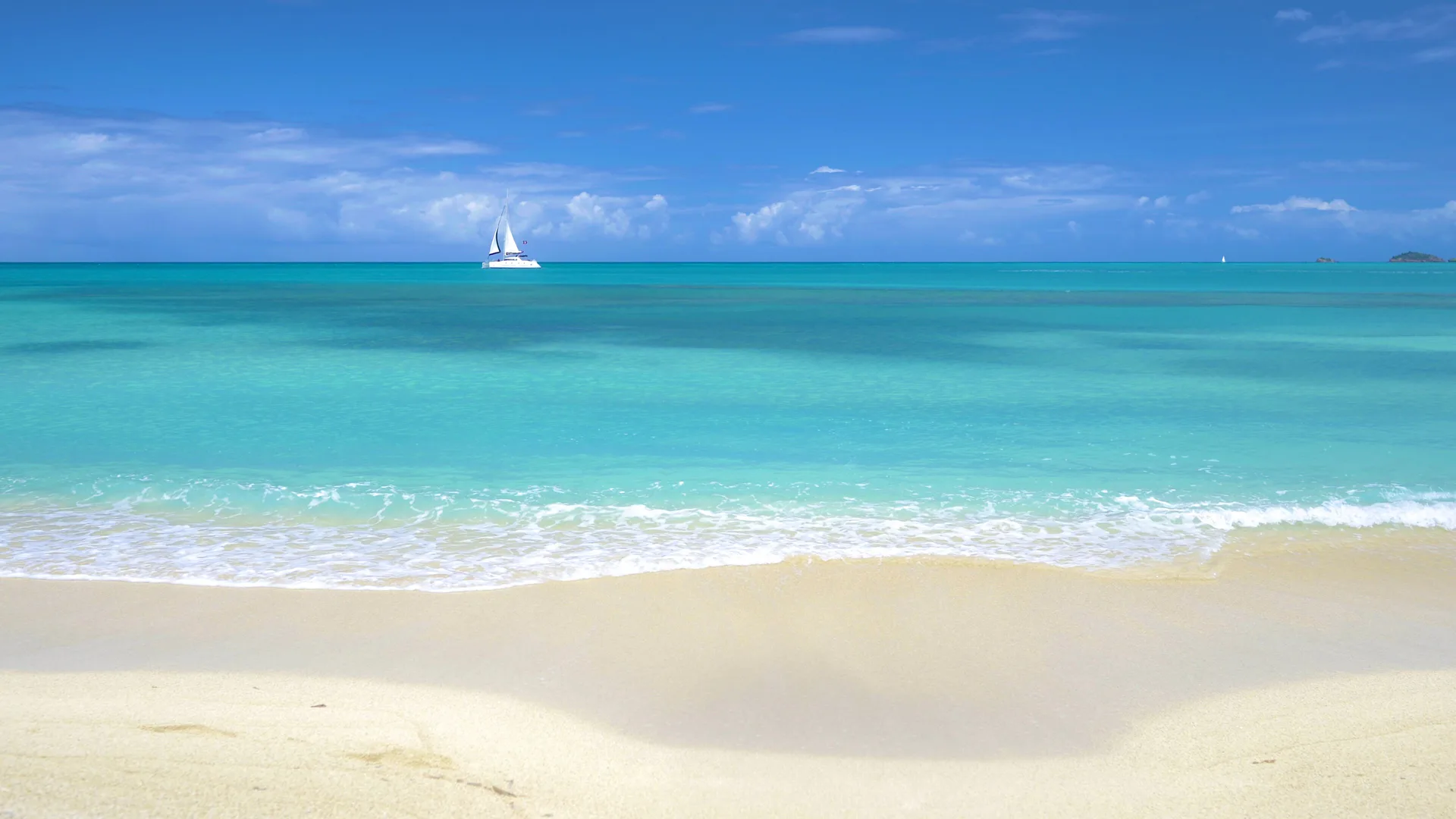 A calm turquoise beach with a sailboat offshore at Cocobay Resort.