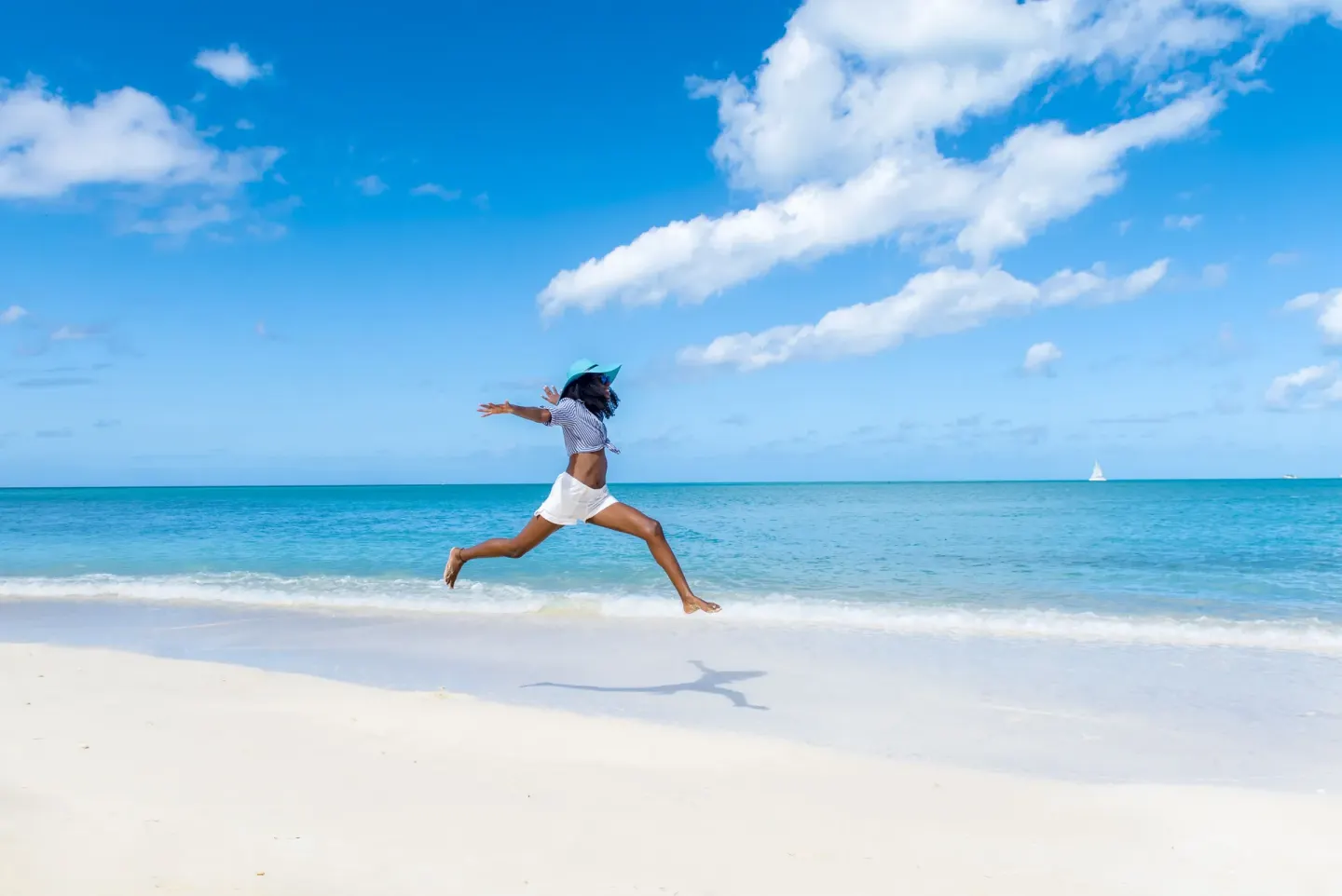 A woman jumps above a white-sand beach and turquoise sea at Cocobay Resort.