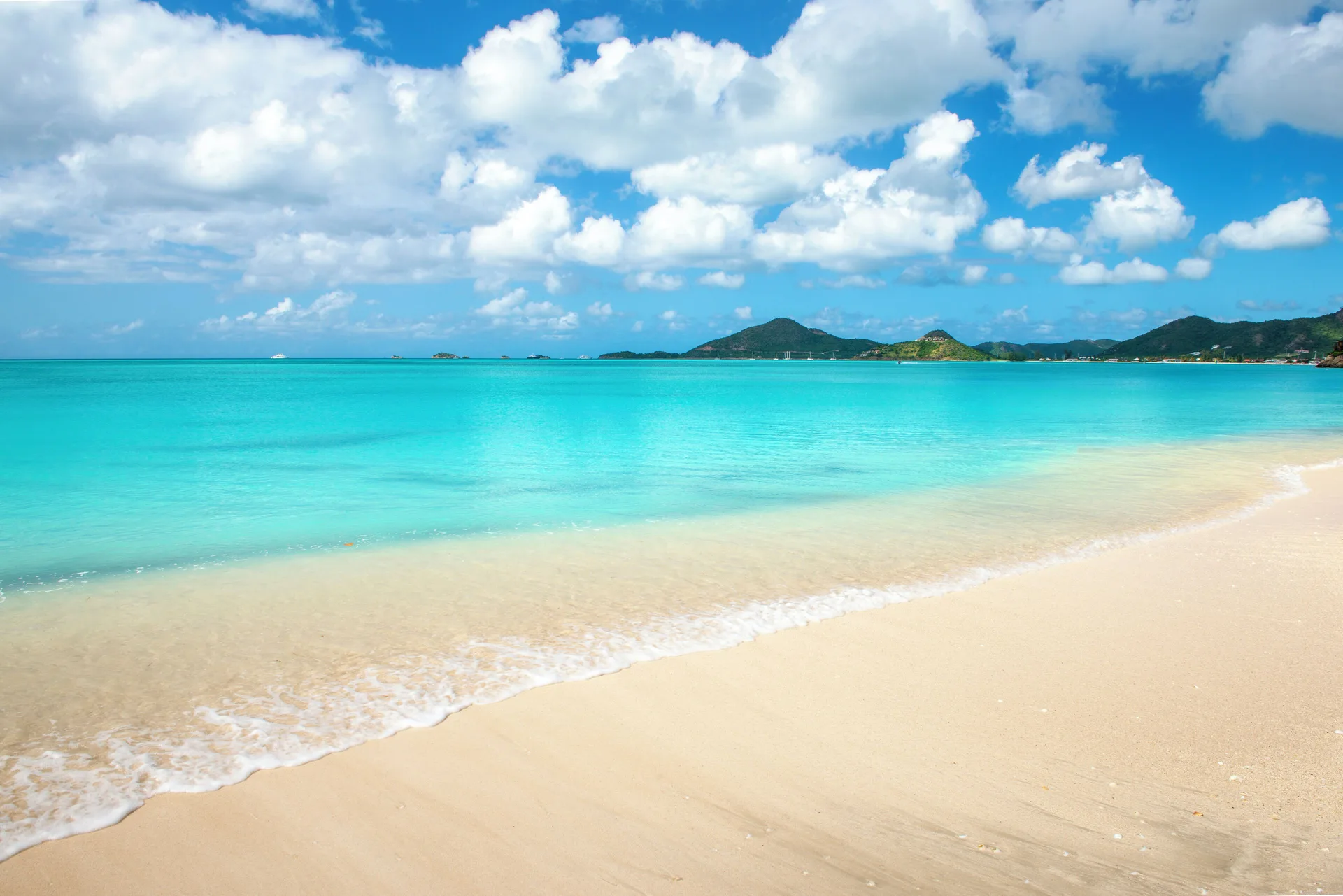 A wide sandy beach and turquoise sea under a cloud-filled sky at Cocobay Resort.