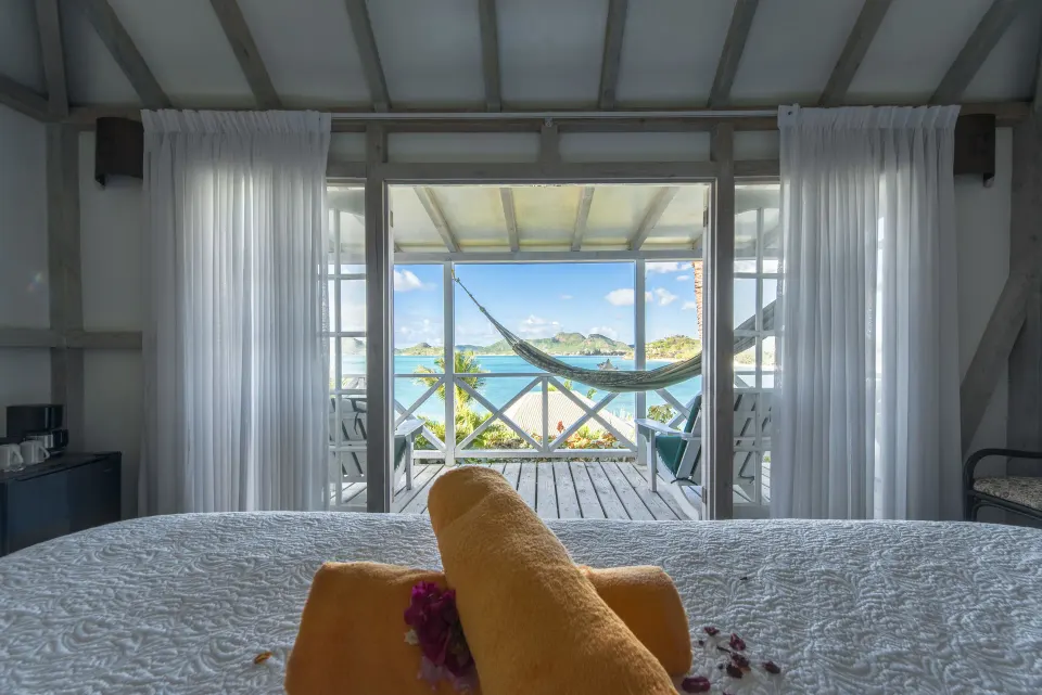 Deluxe Cottage bed at Cocobay Resort facing a veranda hammock and ocean view.