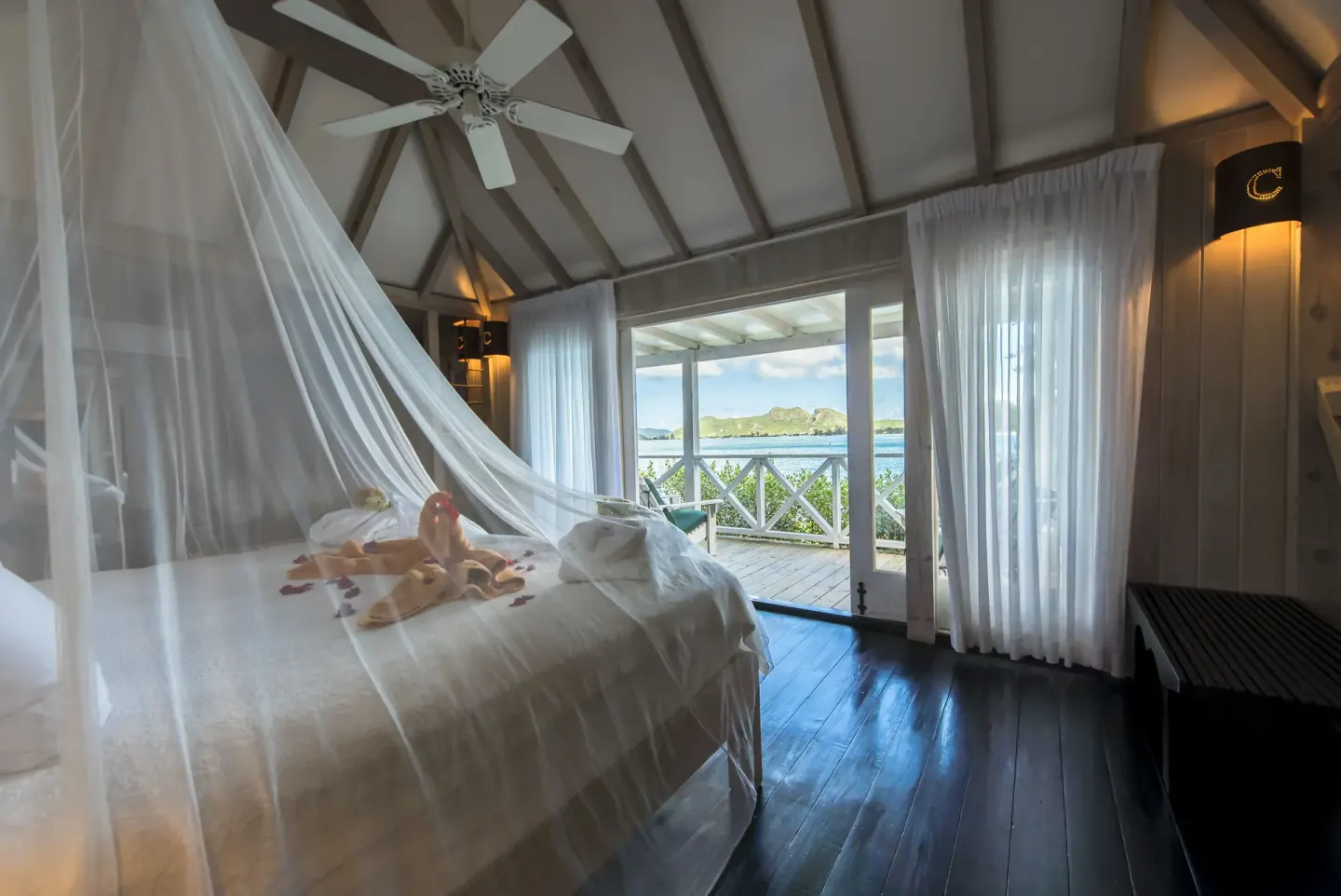 Deluxe Cottage king bed at Cocobay Resort with netting and balcony doors facing the water.