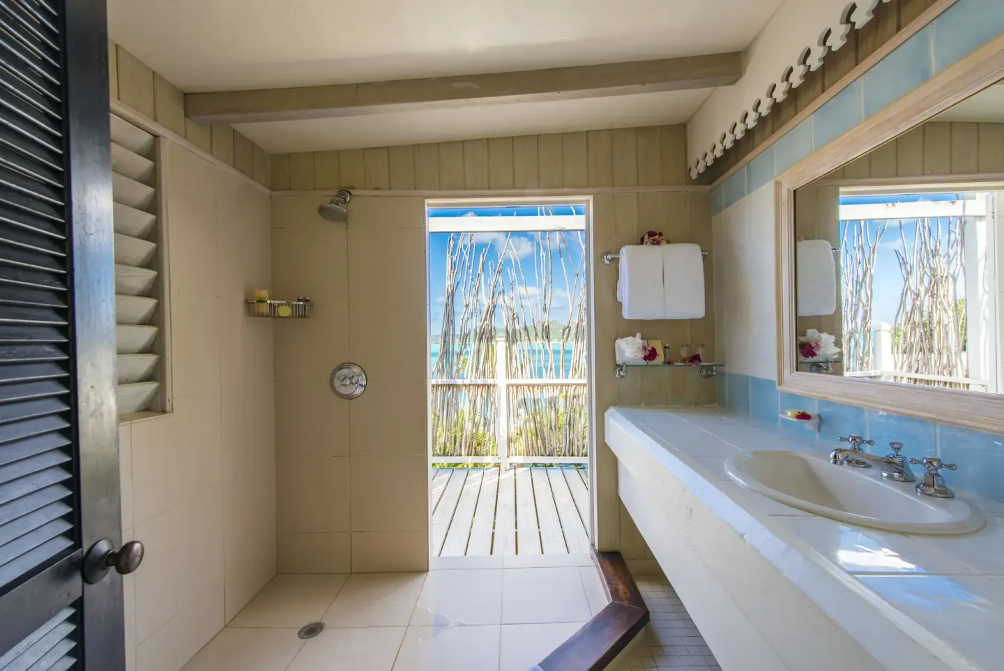 Deluxe Cottage bathroom at Cocobay Resort with shower, sink, mirror, and ocean-facing doorway.
