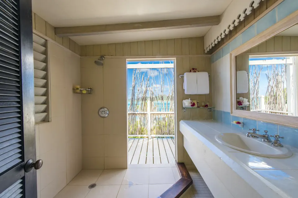 Deluxe Cottage bathroom at Cocobay Resort with shower, sink, mirror, and ocean-facing doorway.