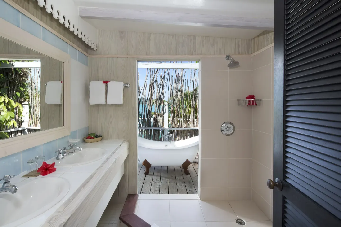 Bathroom at Cocobay Resort with double vanity, open shower, and outdoor tub visible beyond.