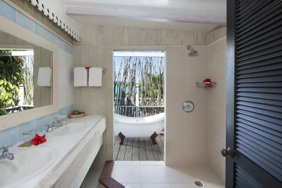 Bathroom at Cocobay Resort with double vanity, open shower, and outdoor tub visible beyond.