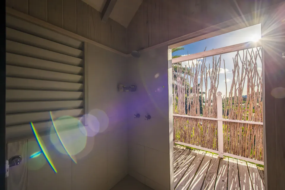 Standard Cottage Garden View shower opening to a sunlit deck at Cocobay Resort.